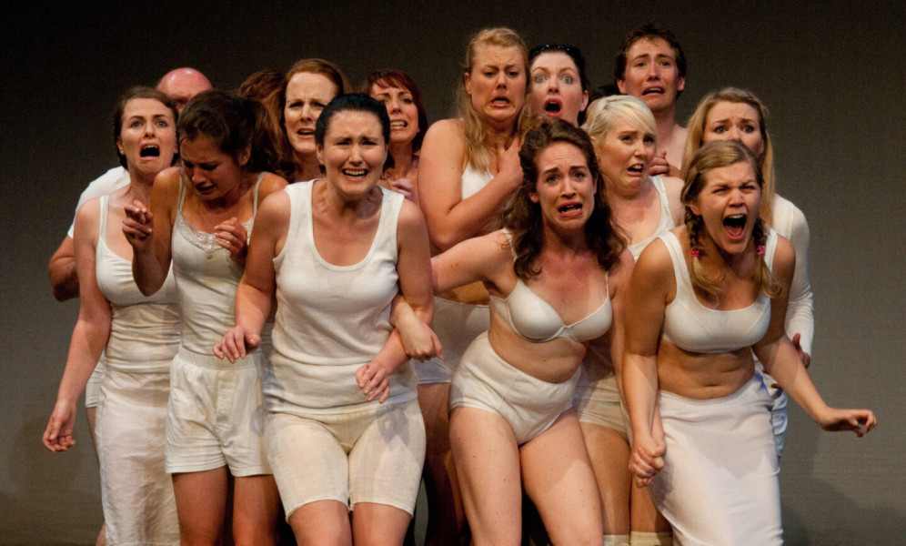 Cetl - a group of 15 performers in white underwear in a tight chorus, all looking variously shocked or angry or upset