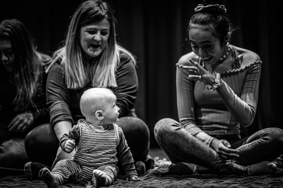 Connect - a young performer waves at a baby who looks intently at her whilst the mother laughs