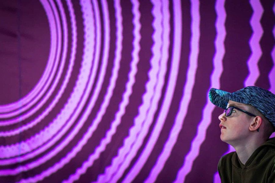 close up of a boy in a cap intently watching a wall full of circles of white light projections