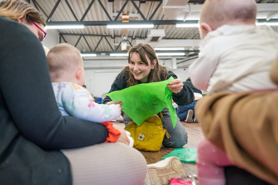 a white woman plays with a baby with a piece of bright green tissue paper