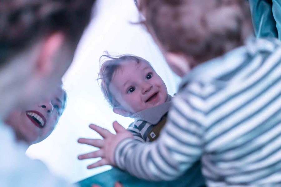 a baby in a striped top looks at itself delightedly in a massive mirror