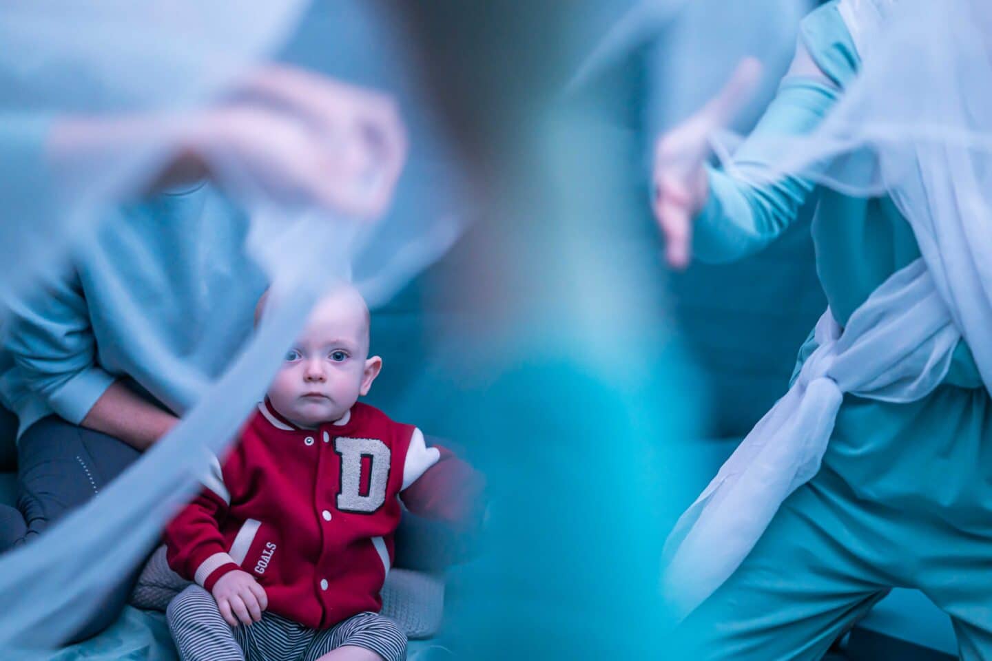 a baby stares at moving chiffons. we can see the vague outline of the performers moving them