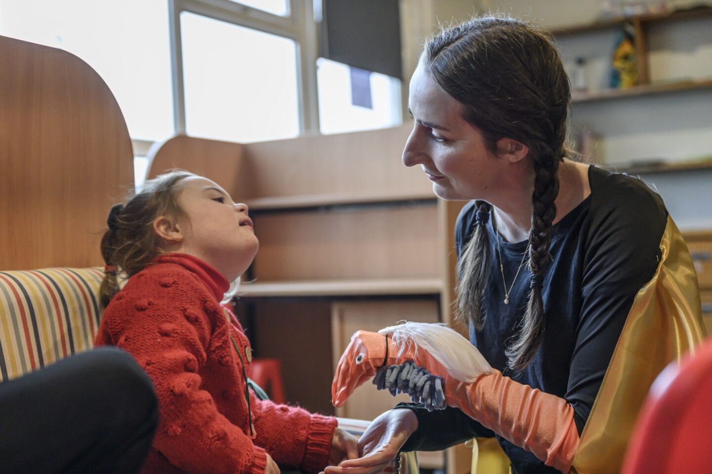 A performer with an orange bird puppet on her arm connects with a young girl. they lock eyes